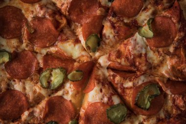 Karanlık taş bir masada salamlı ve salatalıklı lezzetli pizza. Yakın plan.