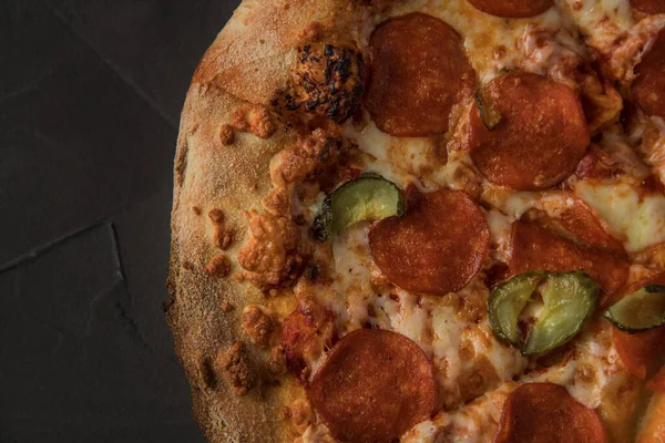 Karanlık taş bir masada salamlı ve salatalıklı lezzetli pizza. Yakın plan.