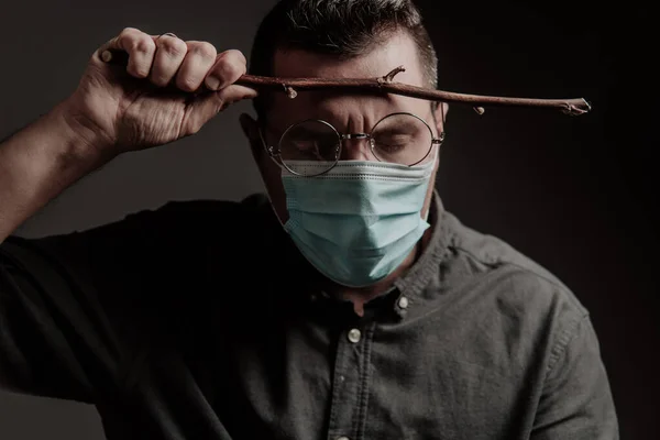 a man in a medical mask and round glasses, with a magic wand on a dark background. The image of the hero from the film
