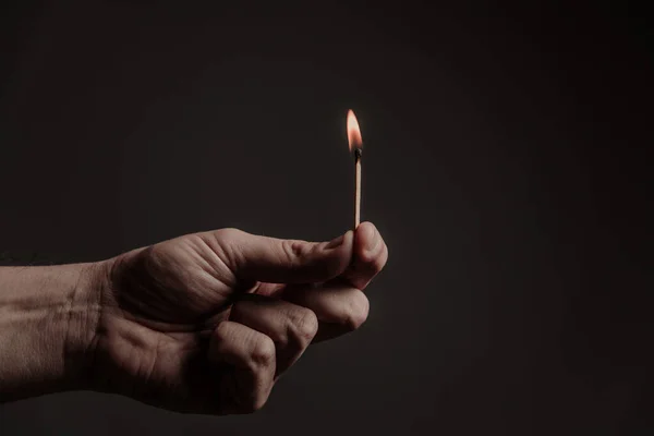 burning match in men's fingers, on a dark background. Close-up