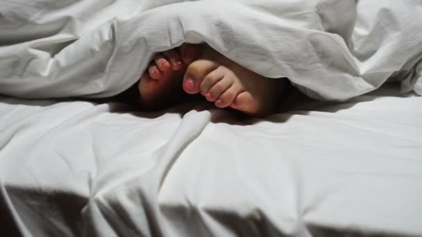 Kvinnliga fötter på den vita sängen under filten — Stockvideo