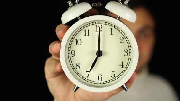 七点钟方向手拿着显示七点钟和铃声的闹钟. — 图库视频影像