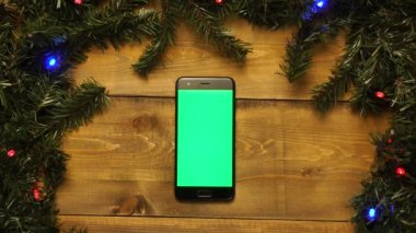 Yeşil ekranlı telefon, göz kırpan çelenklerle süslenmiş ahşap masa..