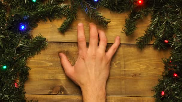 Mão batendo os dedos na mesa de Natal de madeira decorada com guirlandas piscando. — Vídeo de Stock