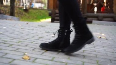 Kadın çizmeleri dökülen yapraklarla kaplı kaldırıma çıkar..