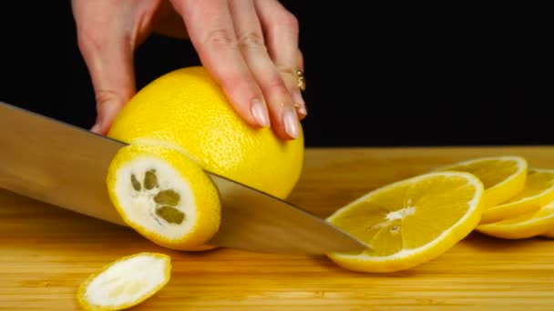 Manos femeninas cortando limón con un cuchillo en una tabla de cortar de madera. Cortar fruta — Vídeos de Stock