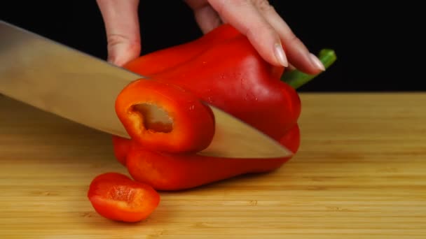 Mãos femininas cortando pimentão vermelho com uma faca em uma tábua de corte de madeira. Cortar legumes — Vídeo de Stock