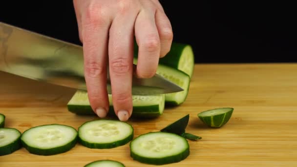 Vrouwelijke handen snijden komkommer met een mes op een houten snijplank. Groenten versnijden — Stockvideo