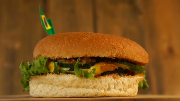 Deliciosa hamburguesa con banderita brasileña encima con palillos. Deliciosa hamburguesa giratoria. — Vídeo de stock
