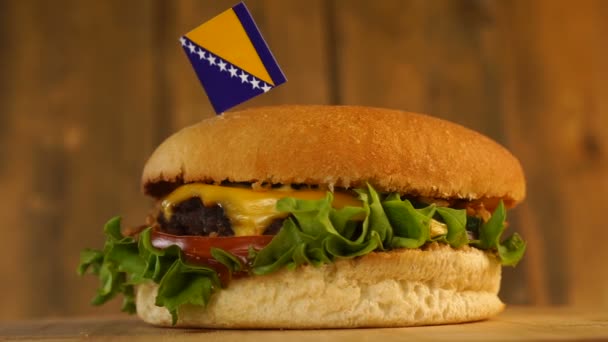 Вкусный бургер с маленьким флагом Боснии и Герцеговины сверху с зубочистками. Вкусный гамбургер вращается. — стоковое видео