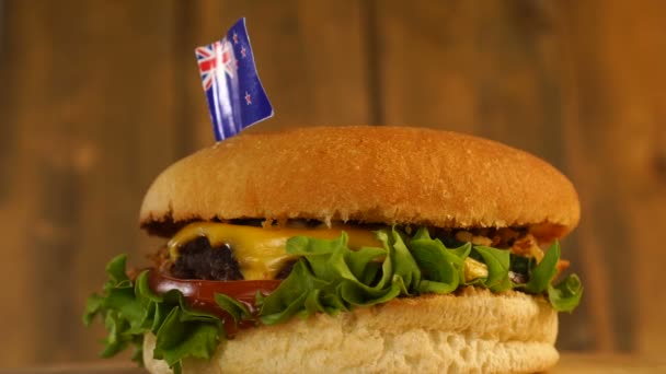 Köstlicher Burger mit einer kleinen Flagge von Neuseeland darüber mit Zahnstochern. Leckere Hamburger rotieren. — Stockvideo