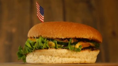 Üzerinde Amerika Birleşik Devletleri 'nin küçük bayrağı olan leziz bir burger. Üstünde kürdan var. Lezzetli hamburger dönüyor..