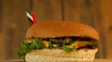 Üstünde kürdanla Birleşik Arap Emirlikleri 'nin küçük bayrağı olan lezzetli bir burger. Lezzetli hamburger dönüyor..