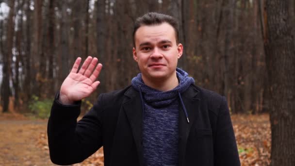 Άνθρωπος κοιτάζοντας κάμερα και χαιρετώντας το χέρι στο πάρκο φθινόπωρο — Αρχείο Βίντεο