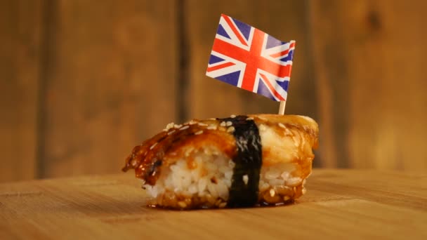 Sushi z rybą, ryżem, wodorostami i małą flagą Zjednoczonego Królestwa na górze obracają się na drewnianym gramofonie. — Wideo stockowe