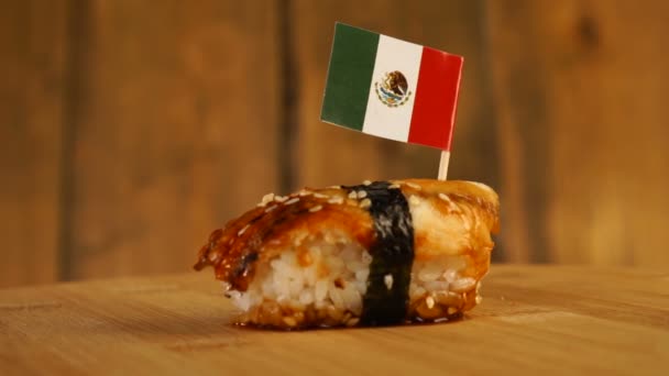 Sushi with fish, rice, seaweed and small flag of Mexico on top rotate on a wooden turntable. — Stock Video