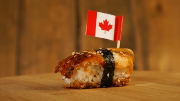 Sushi con pescado, arroz, algas marinas y pequeña bandera de Canadá en la parte superior rotan en un tocadiscos de madera. — Vídeos de Stock