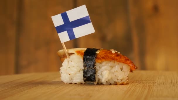 Balık, pirinç, deniz yosunu ve üzerinde Finlandiya 'nın küçük bayrağı bulunan suşi tahta bir döner tablada döner.. — Stok video