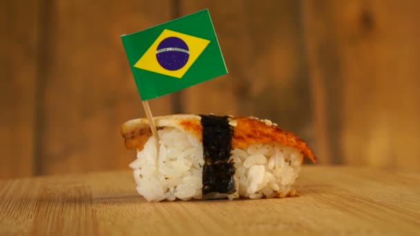 Sushi z rybą, ryżem, wodorostami i małą flagą Brazylii na górze obracają się na drewnianym gramofonie. — Wideo stockowe