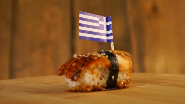 魚、米、海苔、ギリシャの旗を上に乗せた寿司が木製のターンテーブルに回転します。. — ストック動画