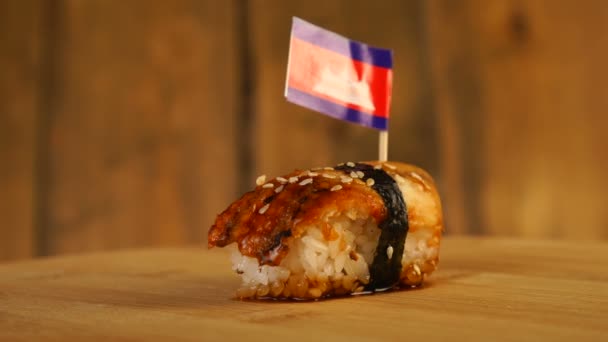 Sushi with fish, rice, seaweed and small flag of Cambodia on top rotate on a wooden turntable. — Stock Video