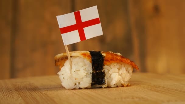 Sushi com peixe, arroz, algas marinhas e pequena bandeira da Inglaterra em cima giram em uma plataforma giratória de madeira. — Vídeo de Stock