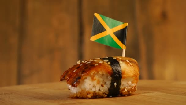 Sushi con pescado, arroz, algas y pequeña bandera de Jamaica en la parte superior rotan en un tocadiscos de madera. — Vídeo de stock