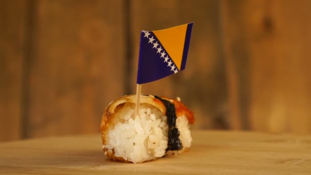 Sushi mit Fisch, Reis, Algen und einer kleinen Flagge von Bosnien und Herzegowina auf einem hölzernen Drehteller. — Stockvideo