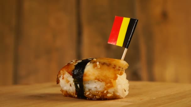 Sushi with fish, rice, seaweed and small flag of Belgium on top rotate on a wooden turntable. — Stock Video