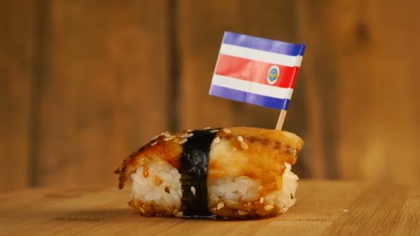 Sushi con pesce, riso, alghe e piccola bandiera della Costa Rica sulla parte superiore ruotano su un giradischi in legno. — Video Stock