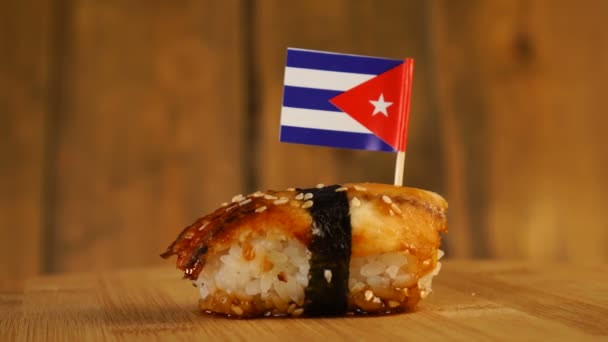 Sushi dengan ikan, beras, rumput laut dan bendera kecil Kuba di atasnya berputar di atas meja putar kayu. — Stok Video