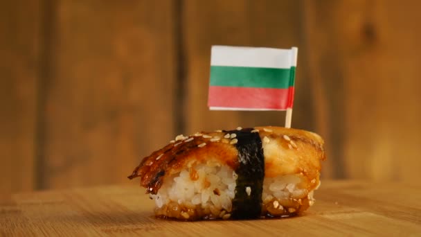 Sushi dengan ikan, beras, rumput laut dan bendera kecil Bulgaria di atasnya berputar di atas meja putar kayu. — Stok Video