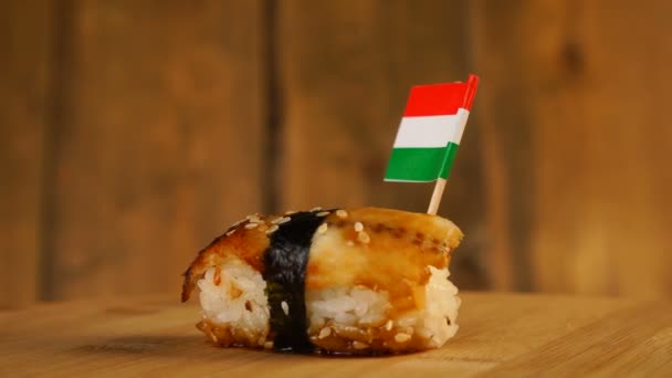 Sushi z rybą, ryżem, wodorostami i małą flagą Węgier na górze obracają się na drewnianym gramofonie. — Wideo stockowe