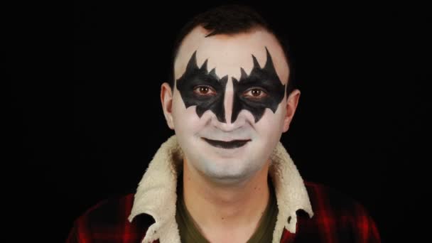 Чоловік в демоні макіяж дивиться і знімає і посміхається на чорному тлі — стокове відео