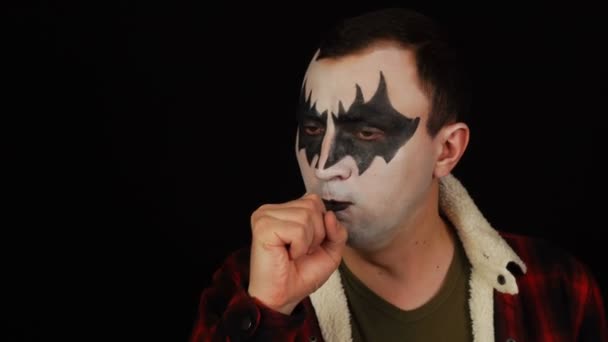 Человек в демоническом макияже страдает от кашля и плохо себя чувствует на черном фоне — стоковое видео