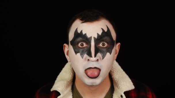 Man in demon make-up maken tonen zijn tong naar camera op zwarte achtergrond — Stockvideo