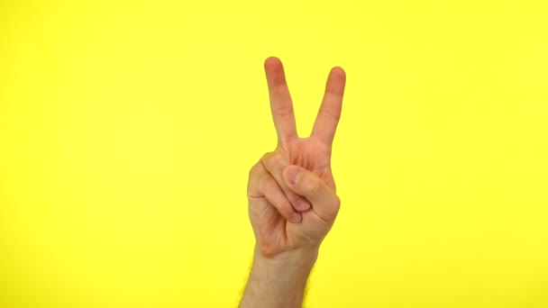 Mans hand showing victory or double on a yellow background. — Stock Video