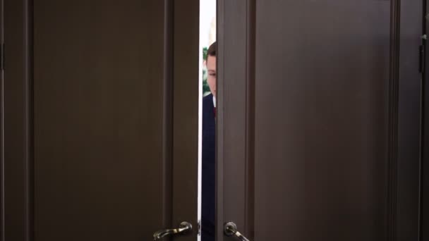 Der Mensch guckt aus der Tür. Kerl schaut durch Türschlitz, schaut sich um und schließt Tür — Stockvideo
