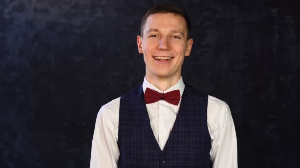 Stijlvolle jongeman in een vest met strikje en een vrolijk gezicht begint te glimlachen — Stockvideo