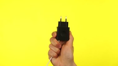 El ele tutuşan akıllı telefon, sarı arka planda şarj oluyor.