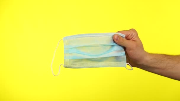 Αρσενικό χέρι κρατά ιατρική μάσκα απομονώνονται σε κίτρινο φόντο. Κλείσιμο βίντεο μόνο με το χέρι — Αρχείο Βίντεο