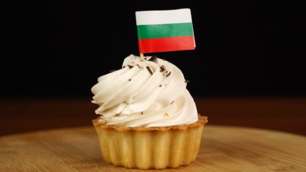 Чоловік кладе декоративний зубочистку з прапором Болгарії в кремовий торт. Національна кухня — стокове відео