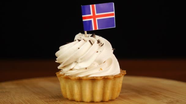 De mens plaatst decoratieve tandenstoker met vlag van IJsland in roomtaart. Nationale keuken — Stockvideo