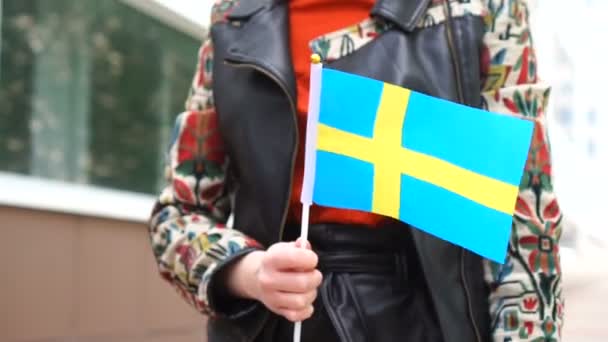 Oigenkännlig kvinna med svensk flagga. Flicka går nerför gatan med Sveriges flagga — Stockvideo