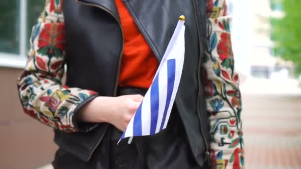 Mulher irreconhecível segurando bandeira uruguaia. Menina andando rua abaixo com bandeira nacional do Uruguai — Vídeo de Stock