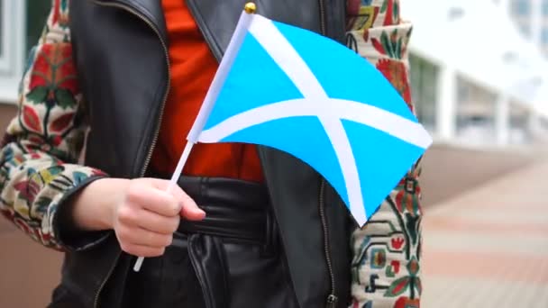 Oigenkännlig kvinna med skotsk flagga. Flicka gå ner gatan med nationell flagga Skottland — Stockvideo