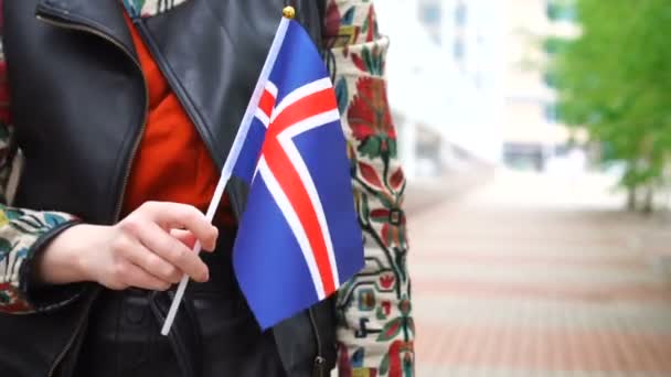 Неузнаваемая женщина с исландским флагом. Девушка, идущая по улице с государственным флагом Исландии — стоковое видео