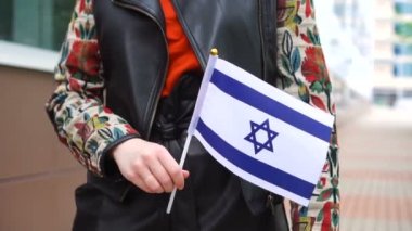 Elinde Yahudi bayrağı tutan tanınmayan bir kadın. İsrail bayrağıyla sokakta yürüyen bir kız.