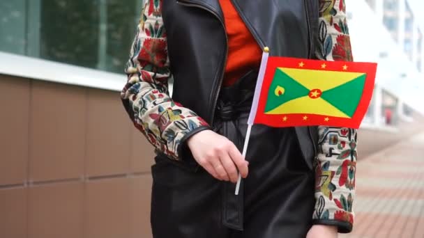 Oigenkännlig kvinna med grenadinsk flagga. Flicka promenader ner gatan med nationell flagga Grenada — Stockvideo