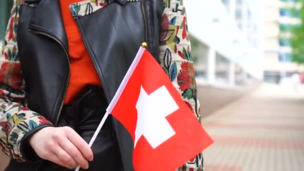 ผู้หญิงที่จําไม่ได้ถือธงสวิส ผู้หญิงเดินลงถนนกับธงแห่งชาติของสวิสเซอร์แลนด์ — วีดีโอสต็อก